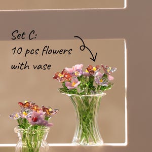 May include: Two glass vases filled with colourful glass flowers. The flowers are pink, orange, and yellow with green stems and leaves. The text "Set C: 10 pcs flowers with vase" is in the upper left corner.