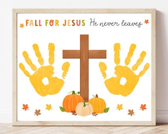 May include: A framed print with the text "FALL FOR JESUS He never leaves." The artwork features a brown cross, orange handprints, and pumpkins. Autumn leaves are scattered around the image, creating a fall theme.