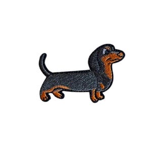 Könnte beinhalten: Gestickter Aufnäher eines Dackelhundes. Der Hund hat einen schwarzen Körper, braune Beine und einen braunen und schwarzen Kopf. Der Aufnäher ist in einem detaillierten, cartoonartigen Stil gestaltet.