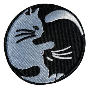 Könnte beinhalten: Runder, gestickter Aufnäher mit einem hellblauen Katzenmotiv auf schwarzem Hintergrund. Die Katze ist in einer spielerischen Pose dargestellt, wobei ihr Schwanz eine Sichel bildet. Der Aufnäher hat ein detailliertes, strukturiertes Aussehen.