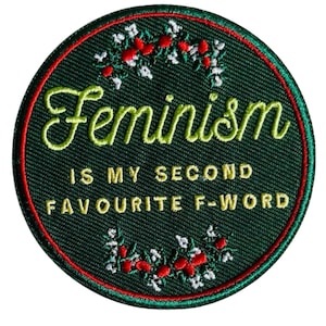 Könnte beinhalten: Runder, gestickter Aufnäher mit dunkelgrünem Hintergrund und rotem Rand. Der Text "Feminism IS MY SECOND FAVOURITE F-WORD" ist in Grün gestickt. Das Design umfasst florale Akzente in Weiß und Rot, die einen dekorativen Effekt erzeugen.