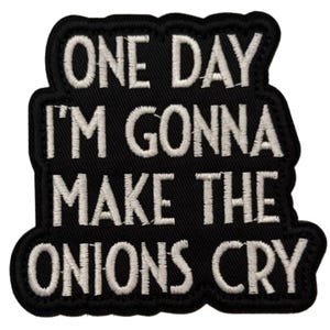 Könnte beinhalten: Schwarzer, bestickter Aufnäher mit dem weißen Schriftzug "ONE DAY I'M GONNA MAKE THE ONIONS CRY". Der Aufnäher hat einen schwarzen Rand mit einem gewellten Rand, zum Aufnähen oder Aufbügeln.