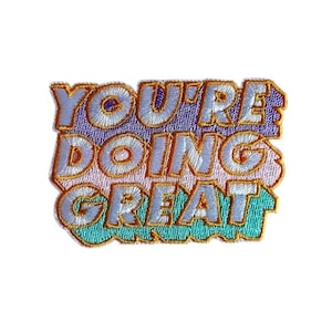 Könnte beinhalten: Gestickter Aufnäher mit den Worten "YOU'RE DOING GREAT" in einem farbenfrohen Design. Der Text ist weiß mit goldenen Umrissen, vor einem lila, rosa und türkisfarbenen Hintergrund.