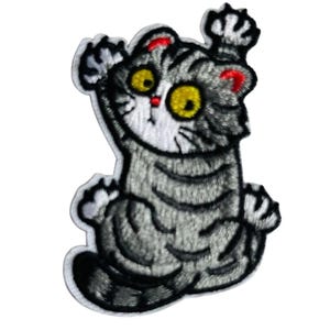 Könnte beinhalten: Gestickter Aufnäher mit einer Cartoon-Katze mit grau-schwarzen Streifen, großen gelben Augen und roten Akzenten an den Ohren. Die Katze befindet sich in einer spielerischen Pose, mit erhobenen Pfoten. Der Aufnäher hat einen weißen Rand.