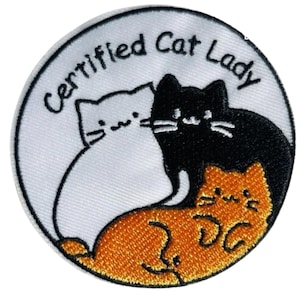 Könnte beinhalten: Gestickter Aufnäher mit weißem Rand. Der Text "Certified Cat Lady" ist oben gewölbt. Er zeigt drei Zeichentrickkatzen: weiß, schwarz und orange, kreisförmig angeordnet.