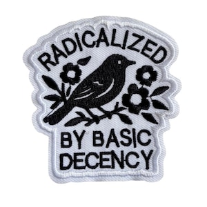 Könnte beinhalten: Ein gestickter Aufnäher mit weißem Hintergrund und schwarzer Stickerei. Das Design zeigt einen Vogel auf einem Ast, umgeben von Blumen. Der Text RADICALIZED ist über dem Vogel gebogen, und BY BASIC DECENCY steht unter dem Vogel.