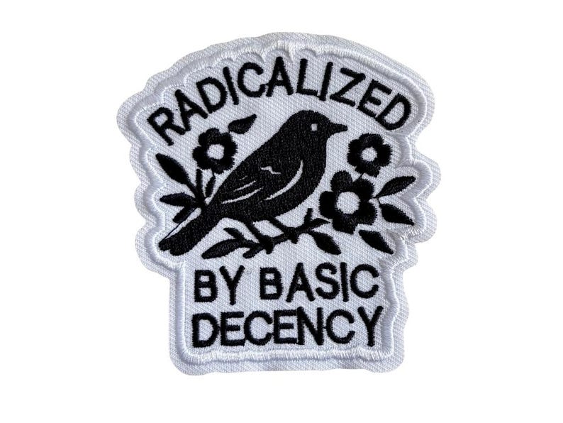 May include: An embroidered patch with a white background and black stitching. The design features a bird perched on a branch surrounded by flowers. The text RADICALIZED is arched above the bird, and BY BASIC DECENCY is printed below the bird.