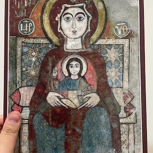 May include: An antique religious icon print featuring a central figure with a halo, holding a smaller figure. The artwork has a vintage aesthetic with muted reds, blues, and gold accents. The image is framed with a dark red border.