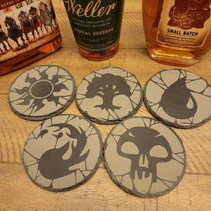 May include: Five round, slate coasters with different Magic: The Gathering symbols. The symbols are a sun, a tree, a teardrop, a flame, and a skull.