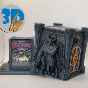 May include: A dark gray, 3D-printed gothic-style box with a detailed demon figure on the front. The box has a hinged door with a pentagram design. Beside it is a smaller box with a comic book cover that reads "Griselbrand".