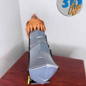 May include: A 3D-printed sword with a gray blade and a brown hilt. The sword has a geometric design and is displayed on a wooden surface. The logo "3D by" is visible in the background.