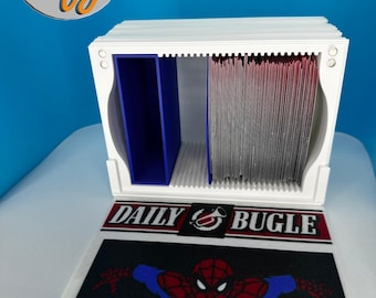 May include: A white 3D-printed card holder with two compartments, one blue and one filled with red cards. The base features a Daily Bugle logo and a Spider-Man graphic. The 3D by logo is in the upper left corner.