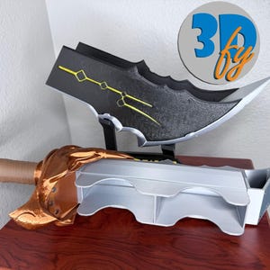 May include: A 3D-printed fantasy sword and blade display. The sword features a bronze-colored hilt and blade guard, with a light gray blade. The blade is black with yellow accents. The logo "3D by" is in a circle in the background.