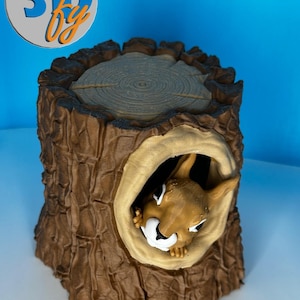 May include: A brown and tan decorative tree stump with a squirrel peeking out of a hole. The top of the stump has a circular design. The logo "3D by" is in the upper left corner.