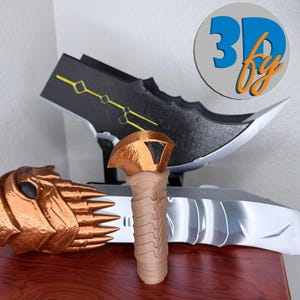 May include: A collection of 3D-printed objects, including a bronze-colored mask, a tan-colored handle, and a black and silver blade with yellow accents. The objects are displayed on a wooden surface. The image includes a logo that says "3D by".