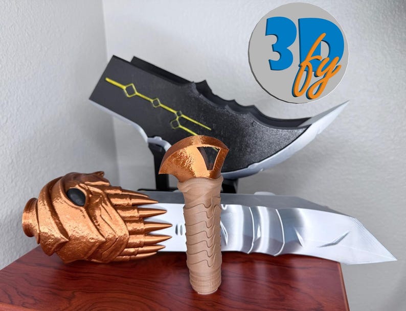 May include: A collection of 3D-printed objects, including a bronze-colored mask, a tan-colored handle, and a black and silver blade with yellow accents. The objects are displayed on a wooden surface. The image includes a logo that says "3D by".