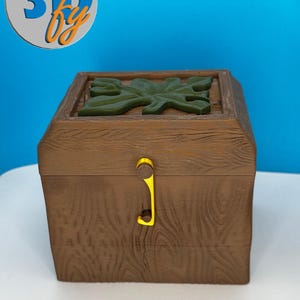 May include: A brown wooden chest with a green leaf design on the lid and a yellow clasp. The chest has a wood grain texture and the text "3D by" in a blue and orange circular logo.
