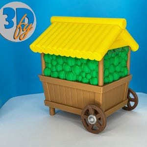 May include: A miniature wooden cart with a yellow roof and green contents. The cart has brown wheels and a brown wooden body. The cart is a 3D printed model. The cart is on a white surface with a blue background.
