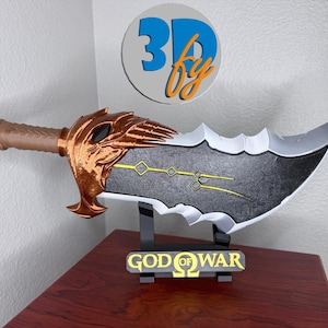 May include: A 3D-printed replica of a sword from the video game God of War. The blade is gray and black with gold accents. The handle is brown and gold. The sword rests on a black stand with the words "GOD OF WAR" in gold.