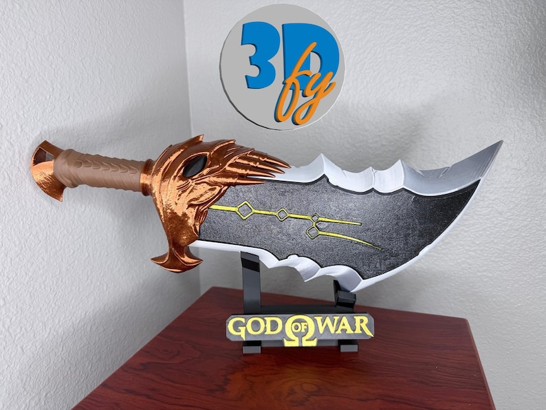May include: A 3D-printed replica of a sword from the video game God of War. The blade is gray and black with gold accents. The handle is brown and gold. The sword rests on a black stand with the words "GOD OF WAR" in gold.