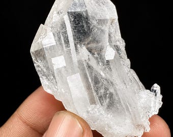 Puede incluir: Un grupo de cristales de cuarzo claro y translúcido que presenta múltiples terminaciones afiladas y puntiagudas, con una estructura superficial compleja y facetada que muestra fracturas internas y estrías visibles en una forma geométrica natural.