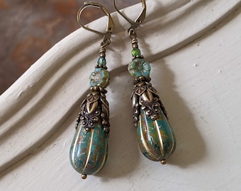 May include: A pair of long, ornate earrings with a vintage aesthetic. The earrings feature teardrop-shaped turquoise and gold-toned beads, accented with floral and filigree metalwork. The top of each earring has a lever back closure and small turquoise and green beads.