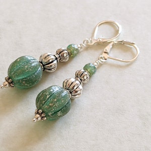 May include: A pair of dangle earrings featuring large, textured, green glass beads with silver-toned accents. The earrings have lever-back closures and smaller green and silver beads.