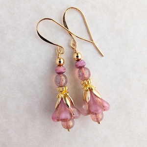 May include: A pair of dangle earrings with gold-colored ear wires. Each earring features a cluster of pink beads, gold-colored accents, and a pink flower-shaped charm. The earrings are designed to resemble flowers.