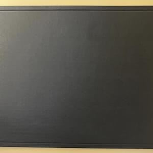 May include: A rectangular, dark gray cutting board with a textured surface and a raised border. The board is set against a light yellow background.