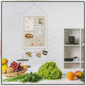 Puede incluir: Un tabl&oacute;n de anuncios con marco blanco con varias tarjetas de recetas y fotos colgadas en una pared de ladrillos blancos. Una cesta de frutas y verduras se encuentra sobre una encimera blanca, con una gran lechuga y naranjas.