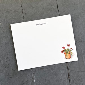 May include: A white card with the name "Maria Avanti" printed in black at the top. A small illustration of a potted plant with red flowers and green leaves is in the bottom right corner.