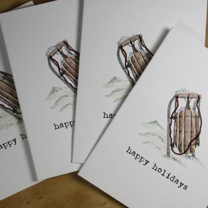 May include: Four white cards with a hand-drawn illustration of a vintage sled on each card. The sleds are brown with red accents and are sitting on a white background with a snowy texture. The text "happy holidays" is printed on the bottom of one card.