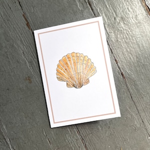 May include: A white card with a brown scallop shell illustration on a light gray wooden surface.
