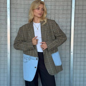 May include: A brown plaid blazer with light blue denim pockets and accents. The blazer has a classic plaid pattern in shades of brown and tan. The pockets are made of light blue denim. The person is wearing a white top and black pants.