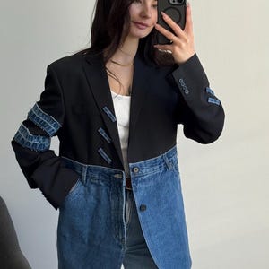 Könnte beinhalten: Ein schwarzer Blazer mit einem unteren Teil aus blauem Denim und Ärmeln, die mit horizontalen Denim-Streifen akzentuiert sind. Das Kleidungsstück verfügt über ein steigendes Revers, einen Knopfverschluss in der Taille und vier Knöpfe an jedem Ärmelabschluss.