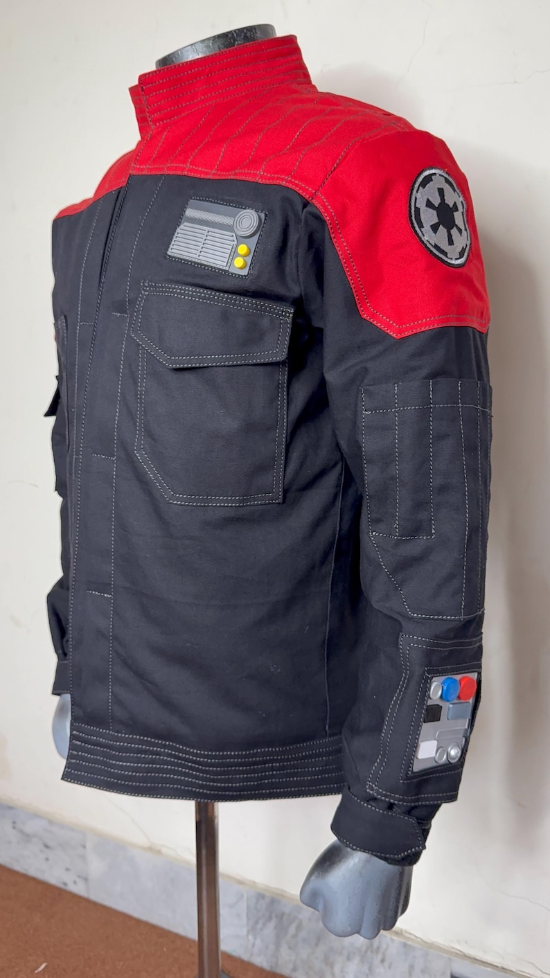 Pode incluir: Casaco preto com detalhes vermelhos nos ombros e design acolchoado. Possui v&aacute;rios bolsos, patches e um emblema circular no ombro. O casaco tem gola alta e &eacute; exibido em um manequim.