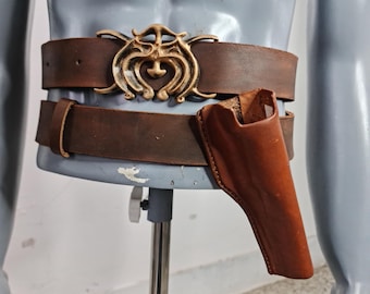 May include: Brown leather belt with a decorative gold-colored buckle. The belt has a matching brown leather holster attached. The belt is displayed on a mannequin.