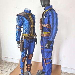 May include: Two blue jumpsuits with brown leather accents and straps. The jumpsuits are on mannequins and have a futuristic design.