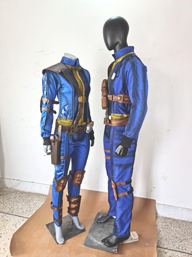 May include: Two blue jumpsuits with brown leather accents and straps. The jumpsuits are on mannequins and have a futuristic design.