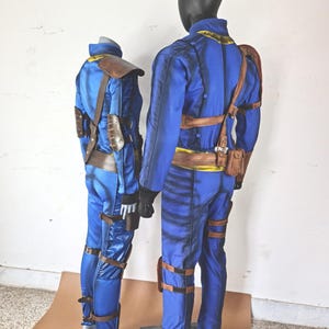 May include: Two blue and brown jumpsuits with yellow accents. The jumpsuits have straps and buckles. The jumpsuits are on mannequins.