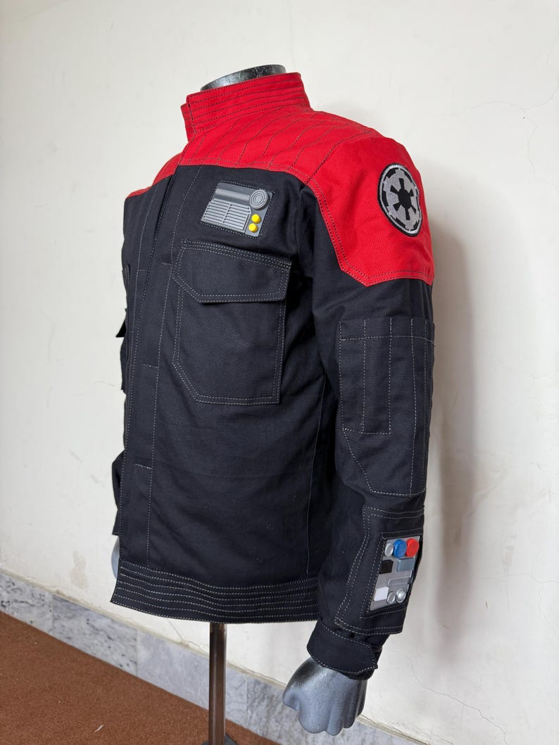 Pode incluir: Casaco preto e vermelho com v&aacute;rios bolsos e patches. O casaco apresenta uma gola alta e um patch no ombro com um emblema circular. Patches adicionais com designs gr&aacute;ficos est&atilde;o nas mangas. O casaco &eacute; exibido em um manequim.