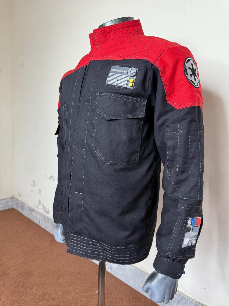Pode incluir: Casaco preto e vermelho com gola alta e v&aacute;rios bolsos. O casaco apresenta um patch no ombro com um emblema circular e outro patch no peito com um design retangular. As mangas t&ecirc;m detalhes adicionais.