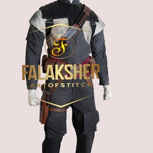 Könnte beinhalten: Ein schwarzes und graues Kostüm, das auf einer Schaufensterpuppe ausgestellt ist. Das Kostüm umfasst eine schwarze Jacke mit Schulterpolstern, eine graue Weste, eine schwarze Hose und einen braunen Gürtel mit Taschen. Der Text "FALAKSHER ARTOFSTITCH" ist sichtbar.