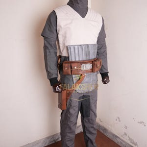 May include: A gray and white costume with a brown leather belt and pouches. The costume includes a vest, pants, and a long-sleeved shirt. The mannequin head is brown. The text "ALAKSHER" is visible on the costume.