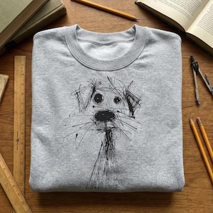 Peut inclure: Un sweat-shirt gris clair avec une illustration noire et esquissée d'un visage de chien. Les yeux, le nez et la bouche du chien sont proéminents, avec des lignes en forme de moustaches s'étendant du museau. Le sweat-shirt a un col rond et des manches longues.