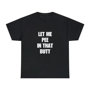 May include: A black short-sleeved t-shirt featuring the white text "LET ME PEE IN THAT BUTT" printed in a bold, sans-serif font across the center of the chest. The garment has a standard crew neckline and a straight hemline at the bottom.