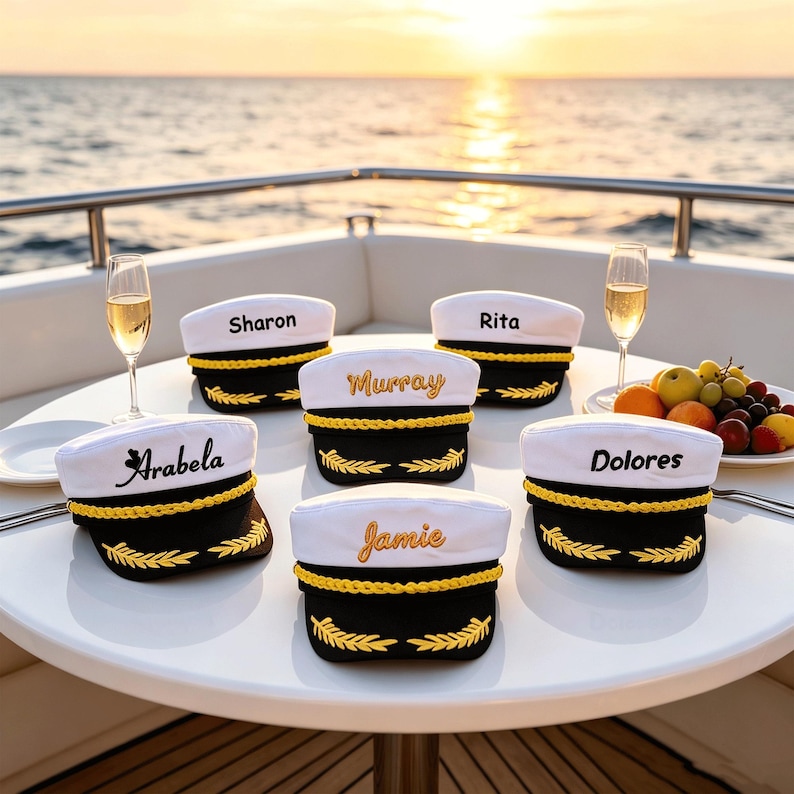 May include: Six white and black captain hats with gold braided trim and gold embroidered laurel leaves on the brim. Each hat features a unique name embroidered on the front: Sharon, Rita, Murray, Arabela, Dolores, and Jamie in various fonts.