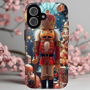 Może przedstawiać: Etui na telefon z motywem Dziadka do Orzechów. Dziadek do Orzechów ma czerwony mundur, złotą koronę i czarny pas. Tło przedstawia choinkę i dekoracje, tworząc świąteczny motyw. Etui ma błyszczące wykończenie i wycięcie na aparat.