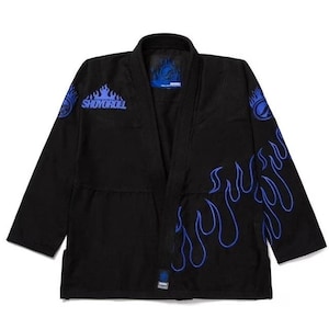 Pode incluir: Kimono de artes marciais preto com detalhes de chamas azuis e logótipo. O kimono apresenta o texto "SHOYOROLL" no peito e desenhos de chamas nas mangas e na lateral. Desenhado para treino e competição de artes marciais.