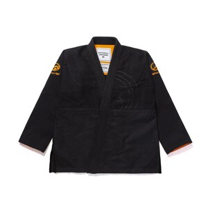 Pode incluir: Uniforme gi Shotoroll preto com detalhes laranja. O gi apresenta logotipos bordados nas mangas e um grande design circular no peito. A gola interior é laranja e o gi é feito de um material durável.